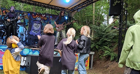 Auf einer Bühn eperformen zwei junge Frauen ihre Musik. Fünf Kinder unterschiedlichen Alterns schauen sie an.