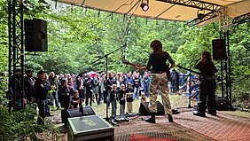 Zwei Frauen performen ihre Musik. Eine kleine bunte Menschenmenge schaut zur Bühne.
